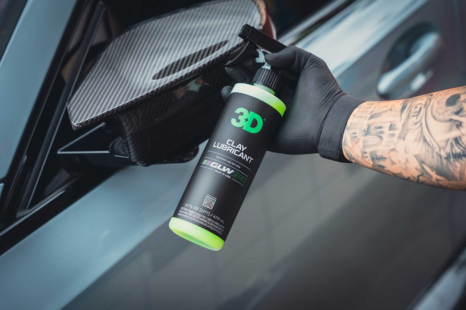 detailer holding bottle of clay lubricant next to carbon fiber mirror cap