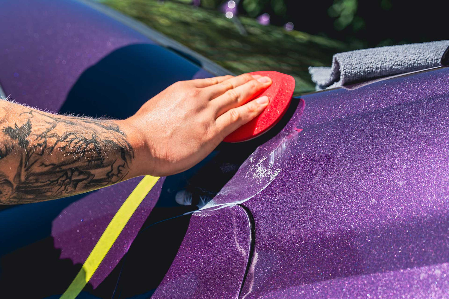 detailing applying ceramic wax to purple car with red applicator pad