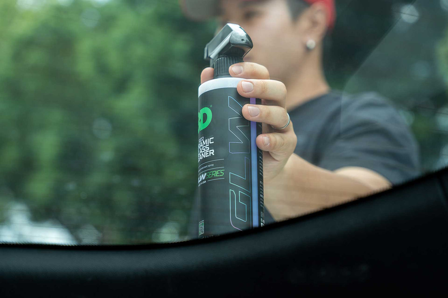 person holding bottle of ceramic glass claner through rear windshield of a car